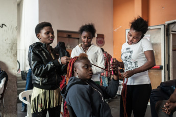 A group of Nigerian girls on the first floor of the orange building arrange their hair according to the typical African style born in the streets, which consists of braiding their hair with coloured cotton threads. Turin.